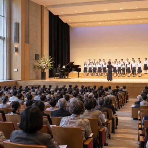 記念式典の舞台で合唱する子どもたちと客席の様子